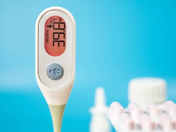 The thermometer for measuring body temperature shows a high temperature. Medical digital thermometer and medicines on a blue background.