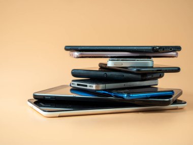 Eski akıllı telefonlar birbirinin üzerine yatar. Bir yığın eski cep telefonu. Turuncu arka planda akıllı telefonlar.