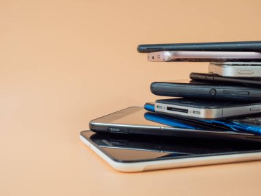Eski akıllı telefonlar birbirinin üzerine yatar. Bir yığın eski cep telefonu. Turuncu arka planda akıllı telefonlar.