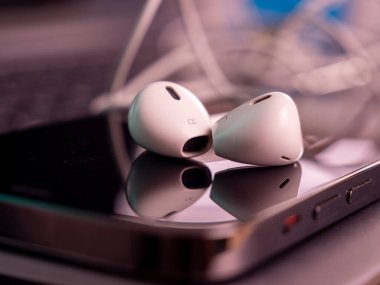 Smartphone has white headphones with a cable. Close-up.
