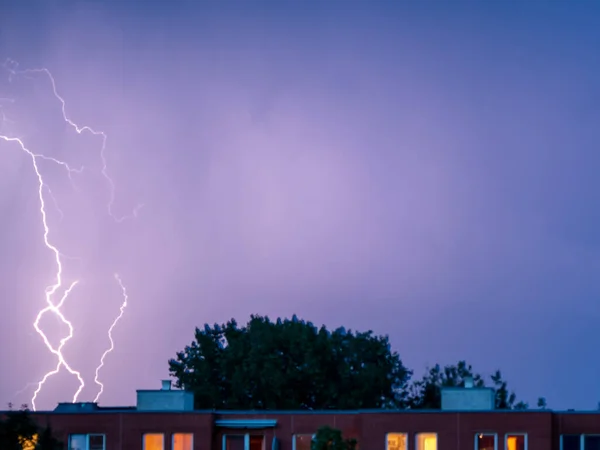 Lightning sparkles over the houses of the city during a thunderstorm. Thunderstorm with lightning. Dramatic mood.
