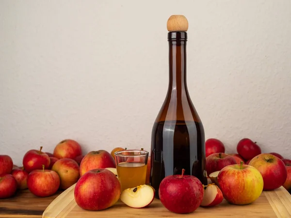 Apple cider vinegar in a bottle with apples against a white wall. Apple cider vinegar and apples.