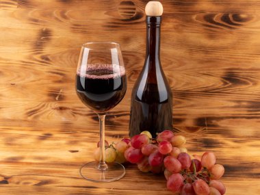 Ahşap arka planda bir bardak şarap, bir şişe şarap ve üzüm. Bardakta şarap..