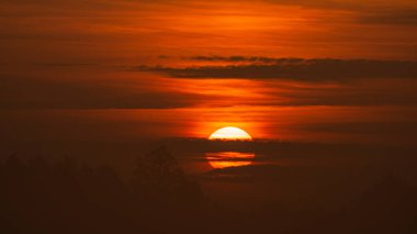 Güzel vahşi gün doğumu ve turuncu bulutlu gökyüzü. Bulutların arkasındaki güneş