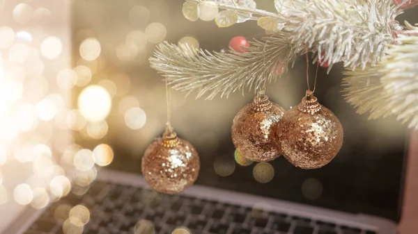 Three golden Christmas tree balls on a fir branch on the background of a laptop and a bokeh , the concept of Christmas 2022 — Stock Photo, Image