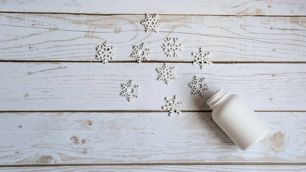 Otwarty słoik na pigułki leży na białym drewnianym tle i małe białe płatki śniegu wylewają się z niego z miejscem na tekst, pojęcie Bożego Narodzenia — Zdjęcie stockowe