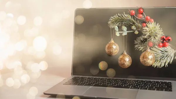 Três bolas de árvore de Natal dourado em um ramo de abeto no fundo de um laptop e um bokeh, o conceito de Natal 2022 — Fotografia de Stock