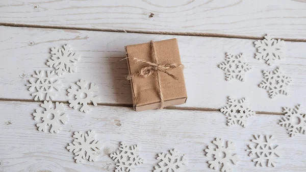 Fondo de madera blanco decorado en los bordes con copos de nieve blancos de madera económica con un pequeño regalo en un paquete de grúa, el concepto de Navidad y vacaciones —  Fotos de Stock