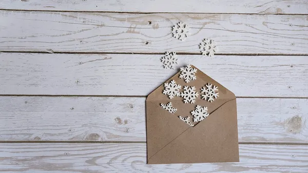 Um envelope de artesanato aberto encontra-se em um fundo de madeira branco e pequenos flocos de neve brancos despeje-o com um lugar para o texto, o conceito de Natal — Fotografia de Stock