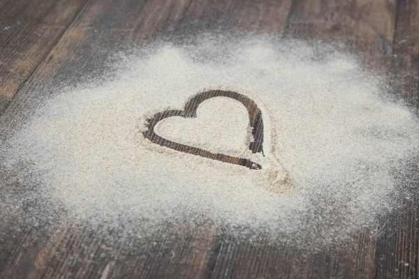 Un corazón pintado sobre harina dispersa sobre un fondo de madera — Foto de Stock