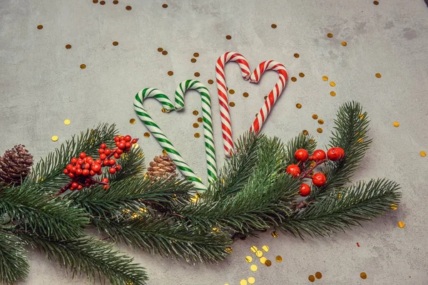 Christmas concrete background with fir twigs and sequins, caramel striped sticks in the shape of a heart christmas concept and christmas sales — Stock Photo, Image