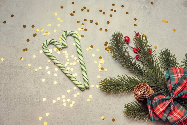 Christmas concrete background with fir twigs and sequins, caramel striped sticks in the shape of a heart christmas concept and christmas sales — Stock Photo, Image