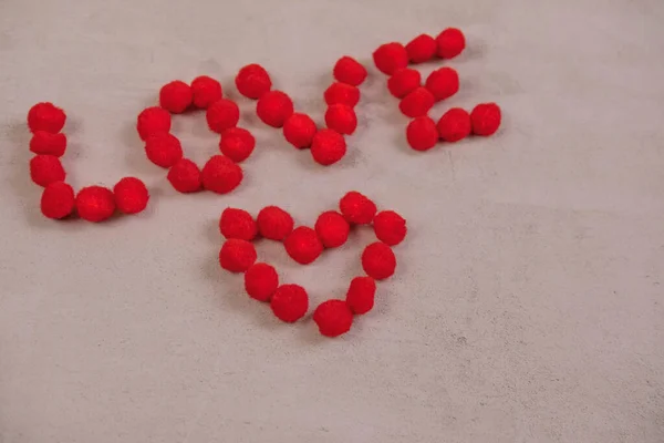 La palabra amor y un corazón hecho de bolas esponjosas sobre un fondo rojo. El concepto del día de San Valentín y todos los amantes — Foto de Stock