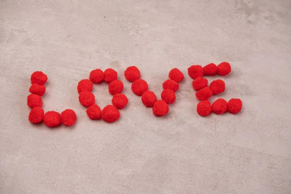 La palabra amor y un corazón hecho de bolas esponjosas sobre un fondo rojo. El concepto del día de San Valentín y todos los amantes — Foto de Stock