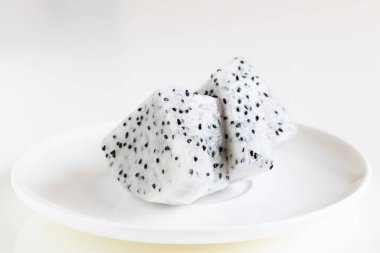 Beyaz masadaki beyaz seramik tabakta soyulmuş ve dilimlenmiş ejderha meyvesi.