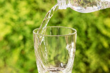 Bulanık yeşil arka planda şişeden cama içme suyu dökülüyor.