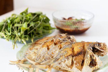 Tabakta bol yağda kızartılmış balık ve sebze sosu beyaz masada, kenar manzaralı seçici odak