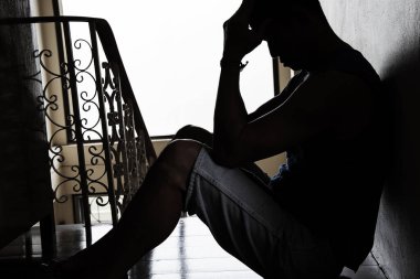 Desperate hopeless man with hands holding head sitting in dark corner 