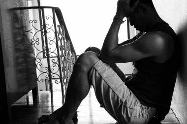 Black and white desperate hopeless man with hands holding head sitting in dark corner 