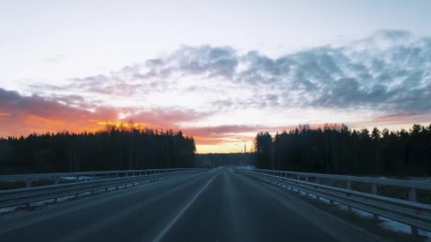 View through the windshield of a moving car on the road with a fence and a beautiful sunrise in the winter sky. — Stock Video