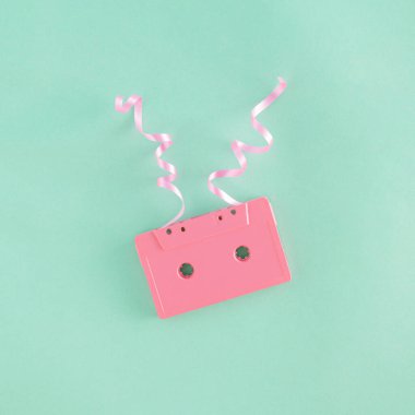 Nane yeşili arka planda pembe kaset ve dekoratif kurdelelerden oluşan yaratıcı bir düzenleme. Minimum retro müzik konsepti. Parti ve kutlama ilhamı.