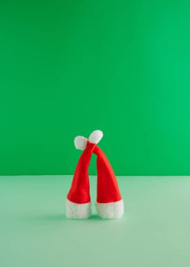 Canlı yeşil arka planda kırmızı Noel şapkalarından yapılmış yaratıcı bir düzenleme. Asgari yeni yıl konsepti. Kucaklaşan bir çift.