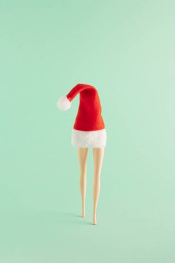 Kırmızı Noel şapkası ve nane yeşili arka planda bacaklardan oluşan yaratıcı bir Noel düzenlemesi. Asgari yeni yıl konsepti. Noel Baba ilham verdi.