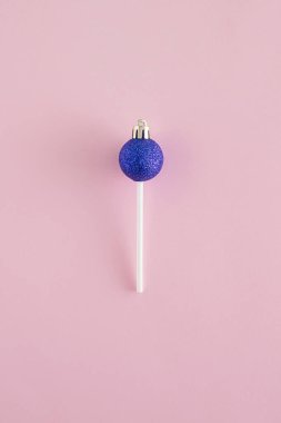 Pastel pembe arka planda canlı mavi Noel süsü ve lolipop çubuğundan yapılmış yaratıcı bir düzenleme. Minimal Yeni Yıl düz konsepti. Şeker ilham kaynağı..