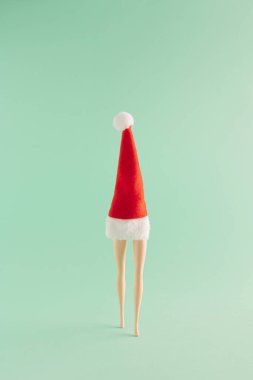 Kırmızı Noel şapkası ve nane yeşili arka planda bacaklardan oluşan yaratıcı bir Noel düzenlemesi. Asgari yeni yıl konsepti. Noel Baba ilham verdi.