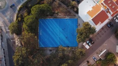 Basketbol sahası hava manzarası. Portekiz 'in Lagos şehrinde ağaçlarla çevrili mavi açık hava sporları sahasında gün batımı uçuşu.