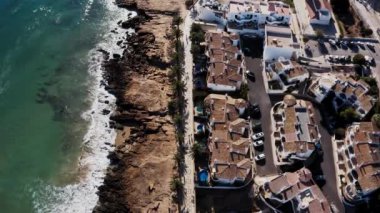 Sinematik Luz sahili hava manzarası. Kıyı şeridi üzerinde güneşli insansız hava aracı uçuşu, güzel evler ve sörfçülerle mavi su..