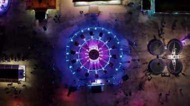 Gece vakti hava manzaralı eyalet fuarı. Portekiz 'deki karnavalda atlıkarıncayla yanıp sönen neon ışıkların üzerinden insansız hava aracı uçuşu.. 