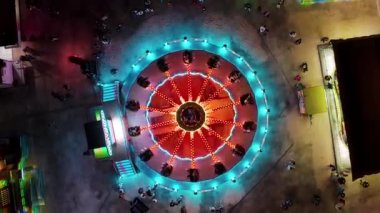Gece vakti hava manzaralı eyalet fuarı. Portekiz 'deki karnavalda atlıkarıncayla yanıp sönen neon ışıkların üzerinden insansız hava aracı uçuşu.. 