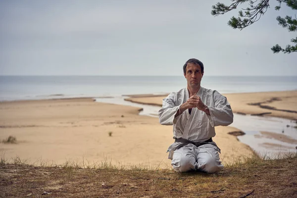 Karate man in an old kimono and black belt meditating at the sea. Martial arts concept. — Stock Photo, Image