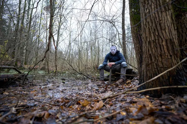 Serial killer Jason Voorhees in hockey mask and machete sitting on the swamp. Friday 13th cosplay costume. — Stock Photo, Image