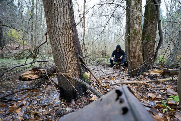 A person in the black hoodie sitting on the swamp. Assassin cosplay costume. — Stock Photo, Image