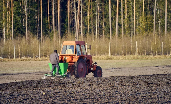 The tractor plows the field, cultivates the soil for sowing grain. Farmer standing behind the tractor during process. The concept of agriculture and agricultural machinery.