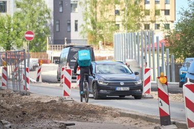 RIGA, LATVIA - MAY 13, 2022. A cyclist from Wolt food delivery company rides against traffic by the road under repair. Hot food deliverer on the bicycle.