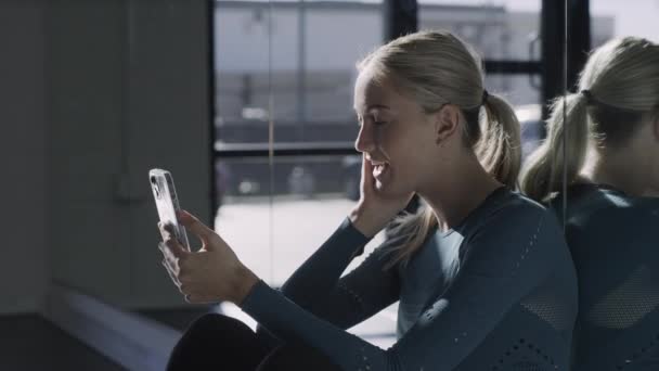 女は床にもたれて座っているミラーウォールビデオチャットオン携帯電話 Lehi ユタ州 アメリカ — ストック動画
