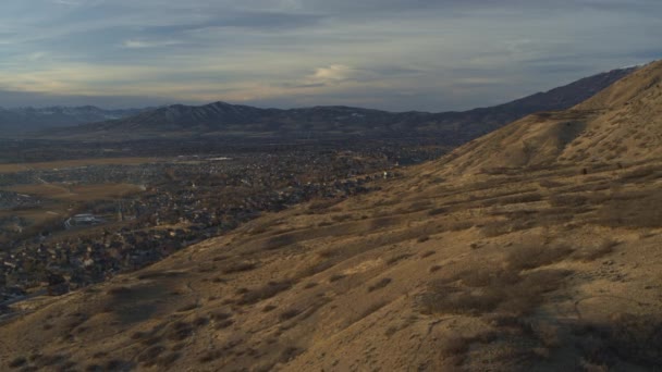 アメリカ合衆国ユタ州のサンセット シーダーヒルズの山の近くの谷の都市の空中フライオーバービュー — ストック動画