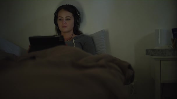 米国ユタ州マーレーの夜 デジタルタブレットで映画を見ながらベッドで女性に傾きます — ストック動画