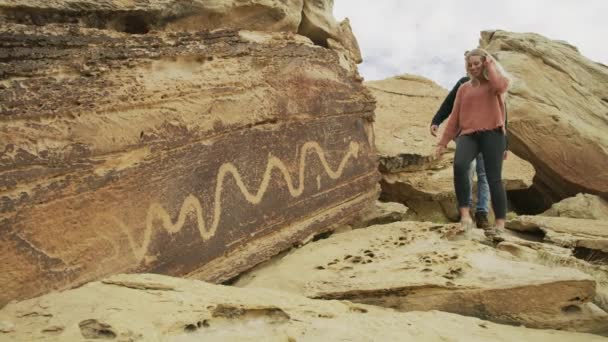 岩の上のカップルハイキングは古代のアートワークを賞賛する Moore ユタ州 アメリカ — ストック動画