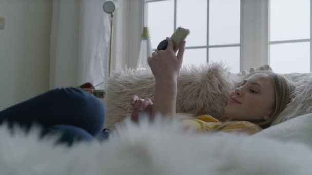 笑いの女の子はベッドの上に寝そべってビデオチャットオン携帯電話 ハイランド ユタ州 アメリカ — ストック動画