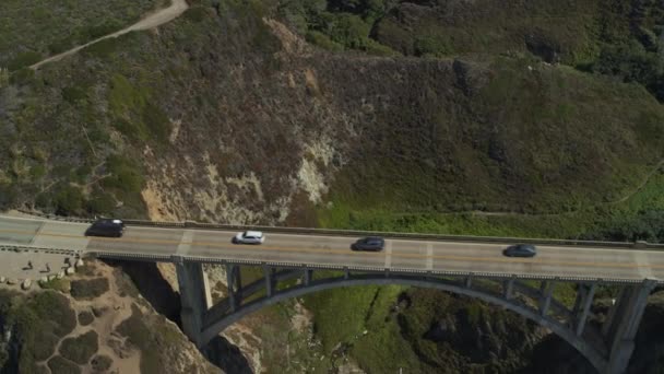 米国カリフォルニア州ビッグサー 波の近くの岩の多い海岸での橋の上を走行する車の空中写真 — ストック動画