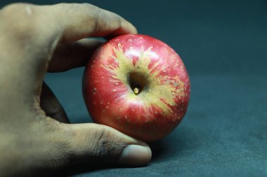 Eller siyah arkaplanda kırmızı bir elma tutuyor.