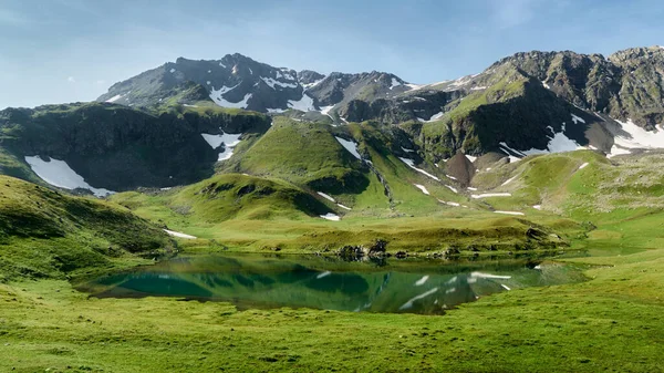 Berglandschaft mit kleinem Gletschersee. Berggipfel mit Schnee, im Vordergrund grünes Gras lizenzfreie Stockbilder