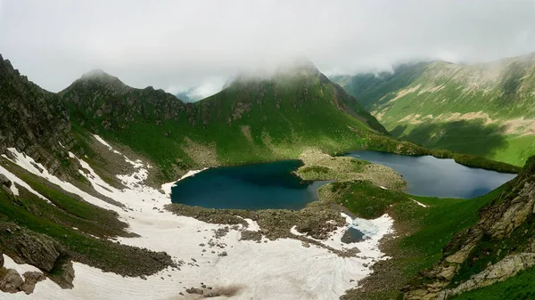 Berglandschaft mit kleinem Gletschersee. Berggipfel mit Schnee, im Vordergrund grünes Gras Stockbild