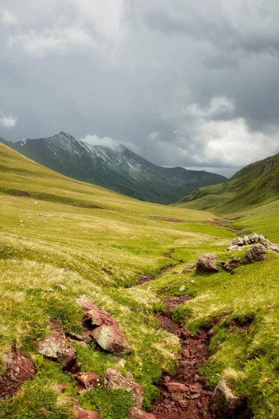 Gebirgsbach fließt über die Steine in einem grünen Tal zwischen den Bergen lizenzfreie Stockfotos