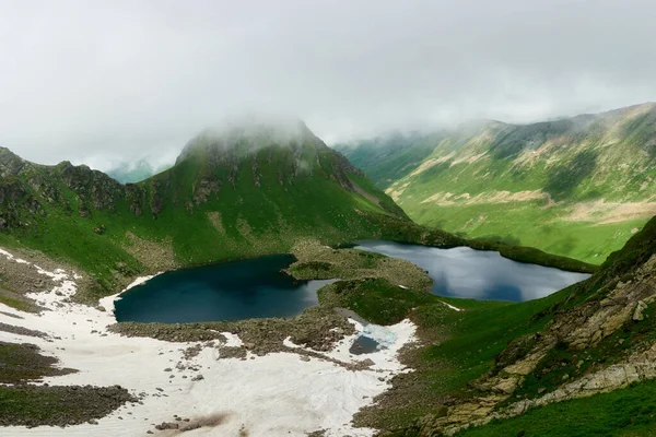 Berglandschaft mit kleinem Gletschersee. Berggipfel mit Schnee, im Vordergrund grünes Gras. Karatschi-Tscherkess Stockbild