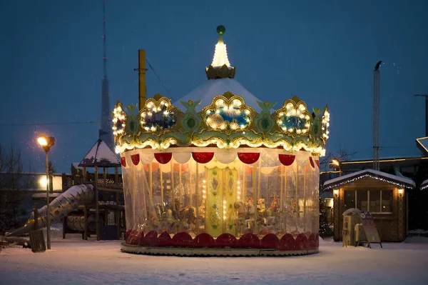 市内の冬の夜 夜の街灯で クリスマス前に点灯し 雪道だ 家は照明で飾られています 子供用のエレガントなカルーセル ラトビア — ストック写真